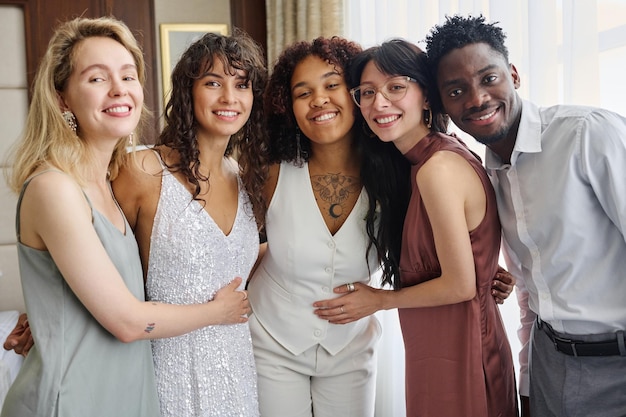 Intercultural group of wedding guests surrounding newlyweds in white attire