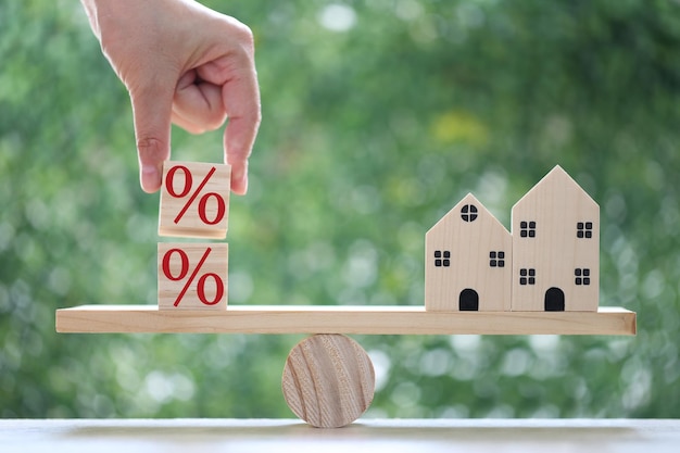 Interest rate up and Banking concept Model house with Percentage symbol icon on wood scale seesaw on natural green background