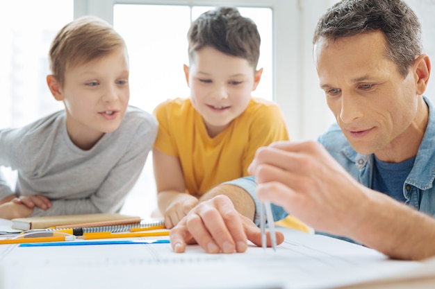 Interesting process. Overjoyed pre-teen boys sitting at the table in fathers office and watching him create the blueprint and measure the distance with the help of a compass