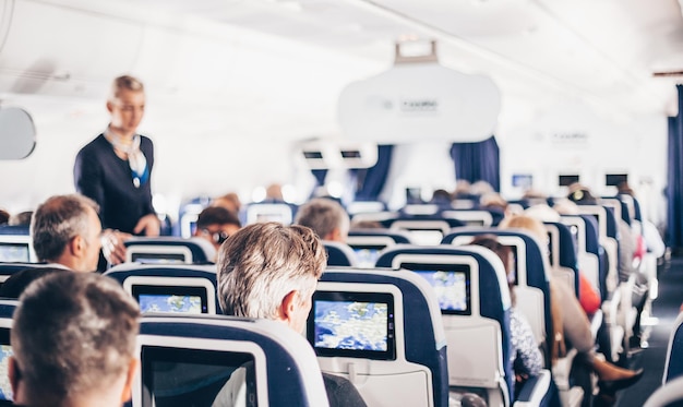 Interior of airplane with passengers on seats and stewardess in uniform walking the aisle serving pe