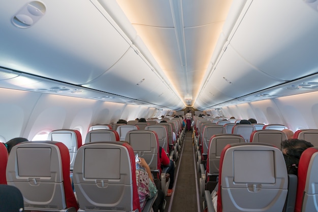 Interior of airplane with passengers on seats and stewardess in uniform walking the aisle.