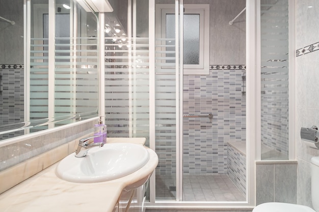 Interior of a bathroom in light blue tiles with shower cabin toilet and sink