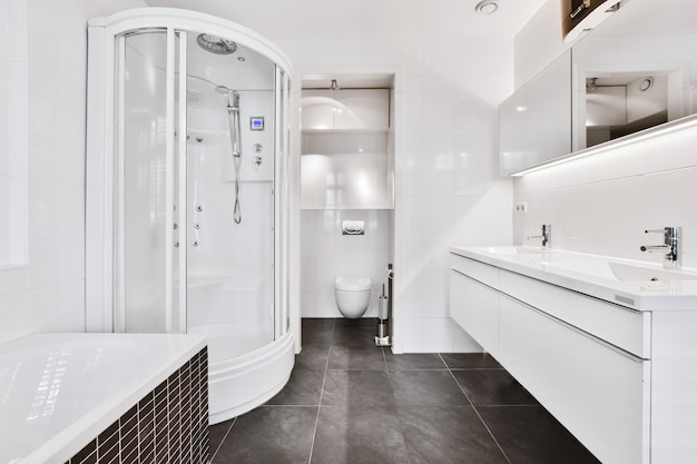 Interior design of modern spacious bathroom with shuttered windows and gray marble floor furnished with white cabinets and mirror in luxury apartment