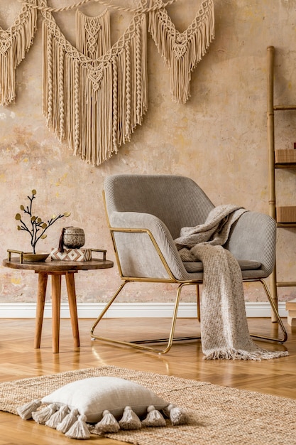 Interior design of oriental living room with modern armchair, macrame, wooden ladder, pillows, decorations and elegant personal accessories in stylish home decor. Wabi sabi wall.