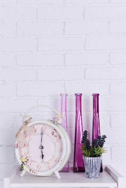 Photo interior design on tabletop with alarm clock plant and decorative vases on white brick wall background