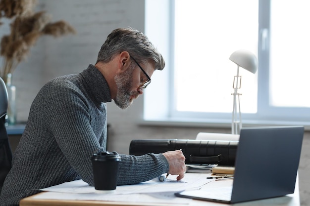 Interior designer working in office with blueprints.Engineer inspect architectural plan, sketching a construction project.Portrait of handsome bearded man at workplace. Business construction concept.