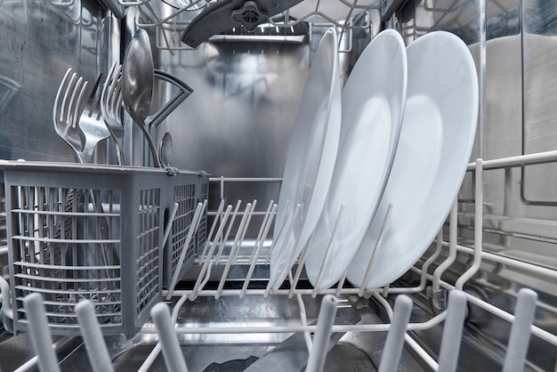 Interior of dishwasher machine with clean dishes after washing.