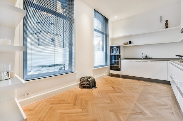 Interior of house kitchen room with white minimalist cabinets and built in appliances and opened passage to dining room with table