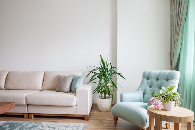 Interior of the living room with white sofa, mint armchair, and a wooden coffee table decorated with plants.