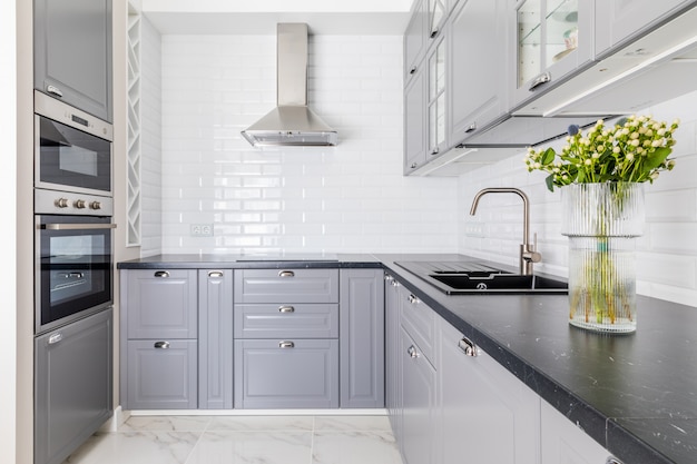 Interior Of The Modern Kitchen. Dark Worktop And Sink, Grey Locker Fronts. Vase With Flowers Decorates The Table