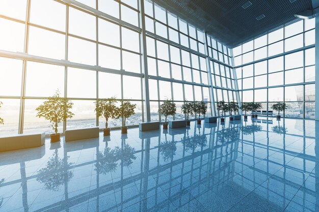 Interior of the modern lobby, terminal or waiting room with glass walls and reflective floor,  natural light and flare