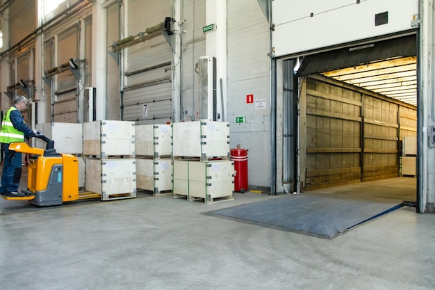 Interior of a modern warehouse storage of retail shop with pallet truck near shelves and loading ramps Storehouse worker in uniform working on forklift