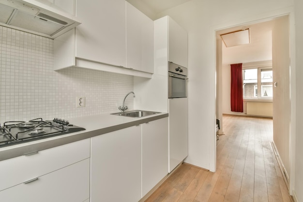 The interior of a small kitchen in white tones with access to the next room in a cozy house