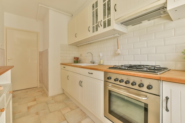 The interior of a small kitchen in white tones with wooden countertops and furniture and tiled floors