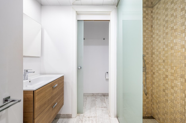 Interior of tiled bathroom with white sink wooden furniture mirror and shower cabin