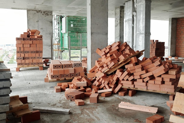 Interior of unfinished block of flats with concrete columns and piles of bricks