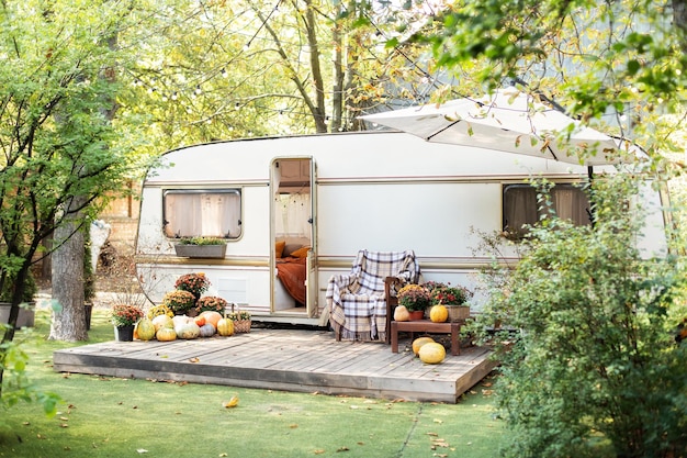 Interior yard campsite with fall flowers potted and pumpkins. RV house porch with garden furniture