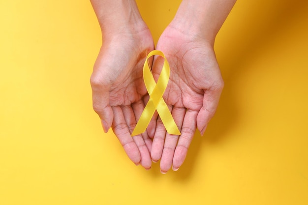 International Childhood Cancer Day. Hands holding yellow gold ribbon. world cancer awareness. 