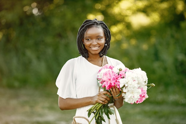 International women's day concept. Happy african american young woman with bunch of peony flowers.