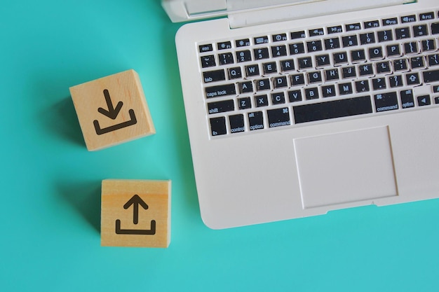 Photo internet and technology concept. top view of laptop and wooden blocks with upload and download icon logo.