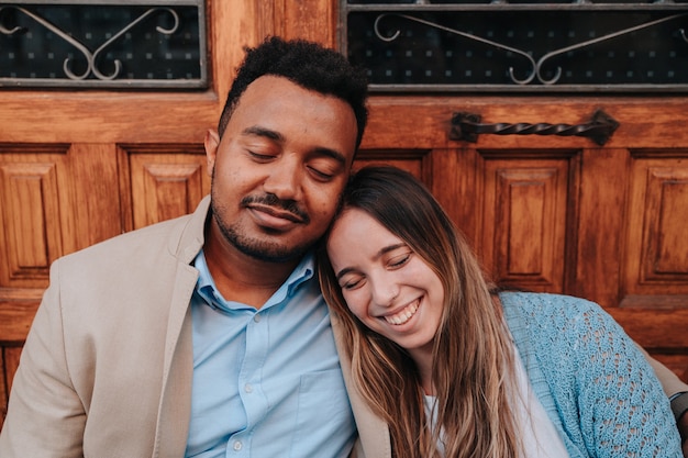 Interracial couple of an African American boy and a Caucasian girl sitting in a doorway while happily closing their eyes