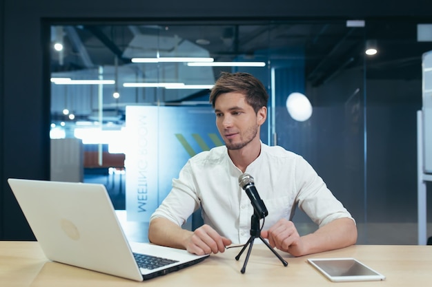 Interview recording Young handsome man sitting at a table in front of a microphone and laptop recording interviews podcasts video lectures He tells gestures