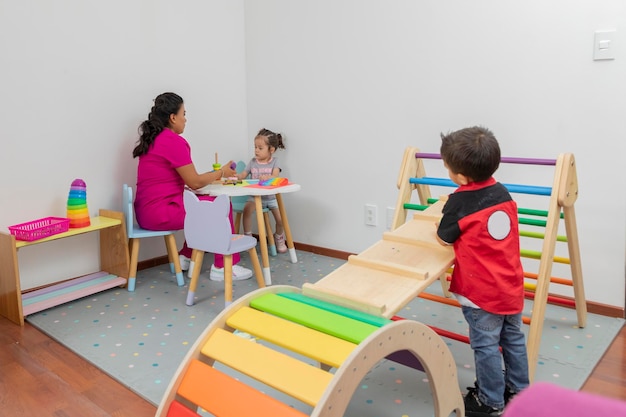 Introverted boy looks from afar at a pediatrician doctor who plays with a girl at a table