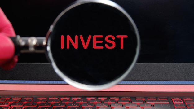 Invest text on the laptop screen through a magnifying glass on a black background