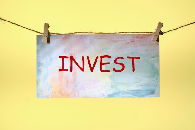 Invest text written on paper suspended from a rope on a yellow background business idea