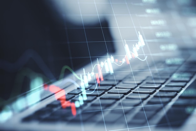 Investing and stock market concept with digital rising up financial chart candlestick on transparent squared screen on modern laptop keyboard background double exposure