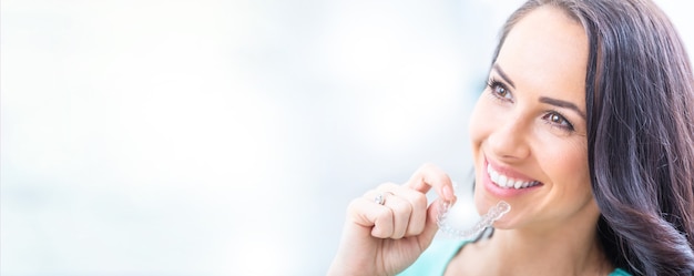 Invisalign orthodontics concept - Young attractive woman holding - using invisible braces or trainer.