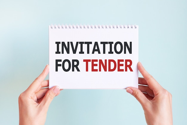 INVITATION FOR TENDER word inscription on white card paper sheet in hands of a woman. Black and red letters on white paper. Business concept.