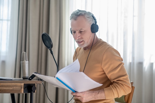 Involved. A gray-haired man in black headphones speaking in microphone and looking interetsed