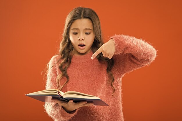 Involved in reading Girl hold book orange background Child show book notepad Book store Free book available read Interesting literature Development and education Child care and happy childhood