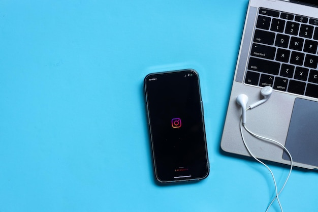 iPhone with Instagram app logo on the screen with earphones and keyboard laptop isolated on blue bac