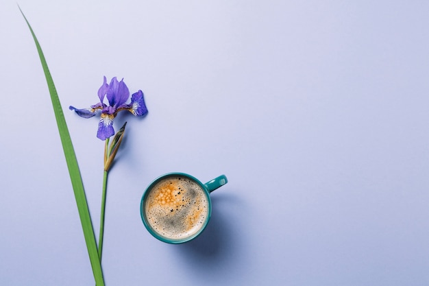 Iris blueflag flower with cup of coffee over purple surface