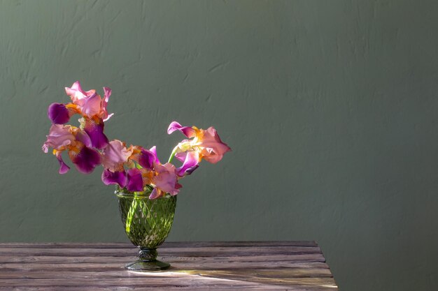 Irises in beautiful glass vase against green wall