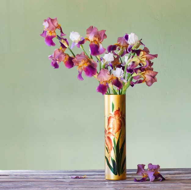 Irises in beautiful glass vase against green wall