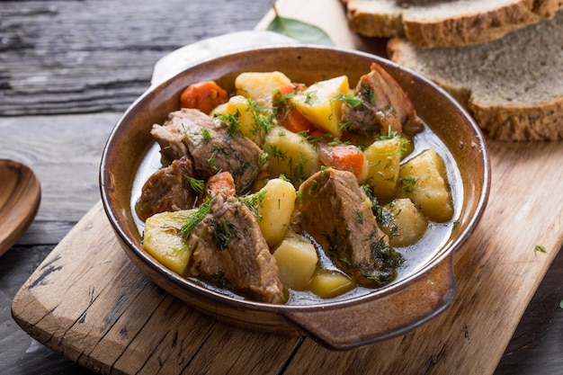 Irish dinner. Beef meat stewed with potatoes, carrots and soda bread on wooden table, top view, copy space. Homemade winter comfort food - slow cooked