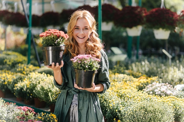 Irish model with bright green expressive eyes and pleasant smile holds in her hands flowerpots with colorful plants Portrait of cute girl with sun rays on her hair