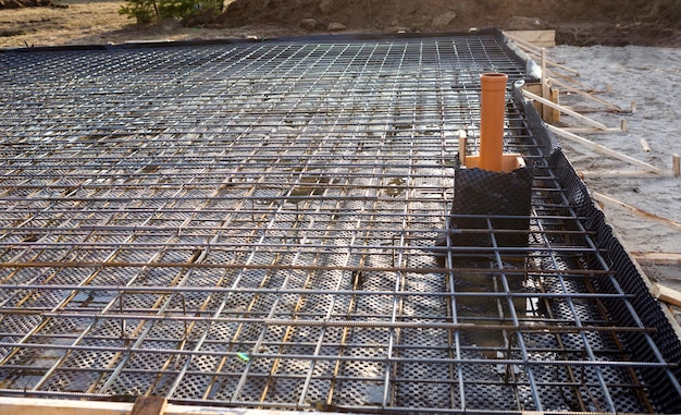 Iron fittings on a wooden formwork with laid pipes are the basis for pouring the foundation of the house with a concrete slab. Construction of cottages, design, engineering communications.