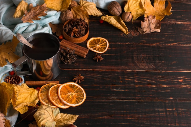 Iron mug with black coffee, spices, dry oranges, on a background of a scarf, dry leaves on a wooden table. Autumn mood, a warming drink. copyspace.