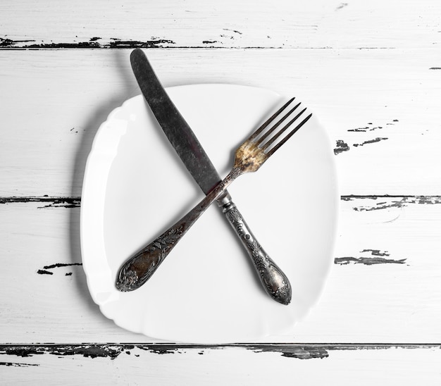 Iron vintage fork with knife lying on a blank white square plate