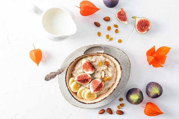 Irregularly shaped ceramic bowl with organic oatmeal porridge with ripe fig wedges and almonds top view white background healthy eating