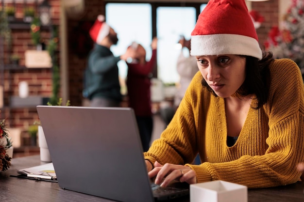 Irritated stressed woman working in noisy office, feeling disturbed by colleagues in workplace decorated with festive holiday ornaments. Tired overworker person in corporate space.