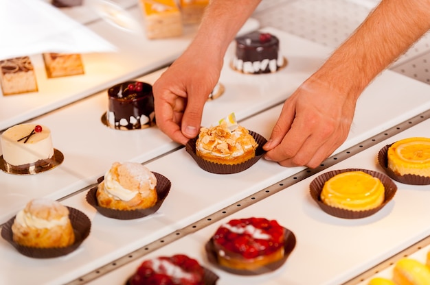 Is this your choice? Close-up of male hand taking a cupcake from showcase while standing in bakery shop