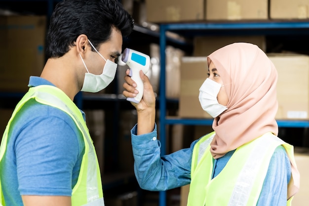 Islam asian warehouse worker taking temperature to worker before getting in factory