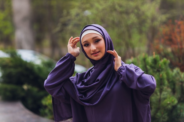 Islamic beautiful woman in a Muslim dress standing on a summer park street background forest autumn trees.world hijab day.