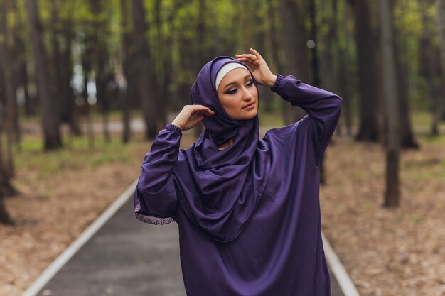 Islamic beautiful woman in a Muslim dress standing on a summer park street background forest autumn trees.world hijab day.