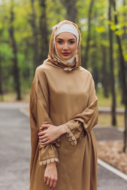 Islamic beautiful woman in a Muslim dress standing on a summer park street background forest autumn trees